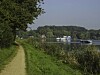 Ausflugsschiff Till auf einem See in Mölln, gesehen von einem Uferweg mit Schilf und bewaldeten Ufern.