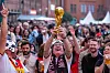 Fußballfans feiern in Berlin; ein jubelnder Fan hält den WM-Pokal über der Menge.