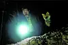 Eine Person leuchtet nachts in bewaldetem Gelände mit einer hellen Taschenlampe.