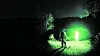 Silhouette einer Person auf einem dunklen Waldweg vor intensiv grün leuchtendem Licht