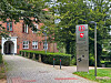 Hinweisschild mit Parkverbotssymbol an einer begrünten Zufahrt vor einem Backsteingebäude