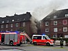 Rauch steigt aus einem Wohnhaus, während Feuerwehrfahrzeuge und Einsatzkräfte davor im Einsatz sind.