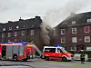 Rauch steigt aus einem Wohnhaus, während Feuerwehrfahrzeuge und Einsatzkräfte davor im Einsatz sind.