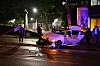 Weißes Auto steht nachts auf nasser Straße, mehrere Personen sichern den Bereich an einer beleuchteten Kreuzung.
