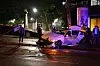Weißes Auto steht nachts auf nasser Straße, mehrere Personen sichern den Bereich an einer beleuchteten Kreuzung.