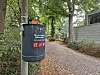Schwarzer Abfallbehälter an einem von Bäumen gesäumten Pflasterweg neben einem Gebäude