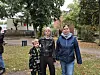 Frau, Mann und Kind stehen im Herbst auf einer Grünfläche zwischen Bäumen und Gebäuden.