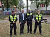 Vier Männer, darunter drei Einsatzkräfte in Warnwesten, stehen auf einer Grünfläche vor Wohnhäusern.