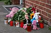 Stofftiere, Blumen und brennende Kerzen liegen vor einem Backsteinhaus zum Gedenken an ein ertrunkenes Kind.