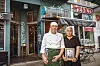 Cengiz Özdemirs Eltern stehen vor dem Bistro Lilly of the Valley; er trägt Kochkleidung, sie hält ein gerahmtes Foto.