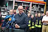 Friedrich Merz spricht in Hürtgenwald-Gey vor Mikrofonen; hinter ihm stehen Einsatzkräfte der Feuerwehr.