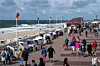 Menschen spazieren auf einer belebten Strandpromenade neben Strandkörben und dem Meer.