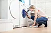 Frau prüft in einem hellen Hauswirtschaftsraum eine geöffnete Waschmaschine.