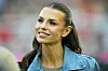 Laura Wontorra steht im RheinEnergieStadion vor verschwommenen Tribünen und lächelt in die Kamera.