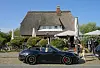 Schwarzer Porsche vor dem Restaurant Rauchfang am Strönwai in Kampen auf Sylt; Passanten stehen daneben.