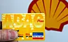 Kraftfahrer hält eine gelbe ADAC-Mitgliedskarte vor dem Shell-Logo an einer Tankstelle.
