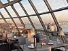 Gäste speisen in einem verglasten Restaurant mit Blick auf die Skyline.