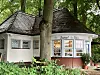 Gartenhaus mit Ziegeldach, Sprossenfenstern und Schriftzug „Sweet & Self“ unter hohen Bäumen