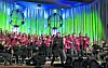 Chor singt auf einer bunt beleuchteten Bühne, während ein Dirigent das Ensemble anleitet.