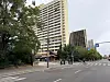 Breite Straße mit Fußgängern, Bäumen und hohen Bürogebäuden an einer Kreuzung