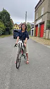 Radfahrerin mit Fahrrad steht auf einer Straße vor einem Gebäude mit roten Toren.