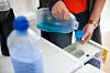 Hände dosieren blaues Waschmittel in die Schublade einer Waschmaschine.