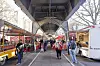 Menschen gehen zwischen Marktständen unter einer Hochbahntrasse entlang.