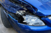 Stark beschädigte Front eines blauen Autos mit eingedrückter Motorhaube und beschädigtem Scheinwerfer
