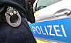 Polizist mit Handschellen und Dienstwaffe vor einem Streifenwagen mit der Aufschrift „POLIZEI“.