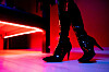 Prostituierte in schwarzen Lackstiefeln steht unter einem Bett im roten Licht eines Studios.