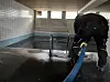 Arbeiter in Schutzkleidung reinigt einen gefliesten Tank mit blauem Schlauch.