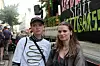 Zwei Personen stehen vor einem Protestbanner, dahinter versammelt sich eine Menschenmenge.