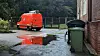 Roter Lieferwagen steht in einer regennassen Hinterhofzufahrt neben einer Mülltonne.