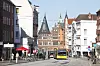 Gelber Bus fährt durch die Holstenstraße in Lübeck vor historischen Backsteinhäusern und dem Holstentor.