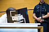 Angeklagte sitzt im Amtsgericht neben einem uniformierten Justizmitarbeiter; ein Monitor verdeckt den Vordergrund.