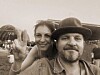 Bärtiger Mann mit Hut und lächelnde Frau posieren bei einer Open-Air-Veranstaltung.