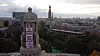 Steinerne Statue auf einem Sockel vor einer dicht bebauten Stadt mit markantem Kirchturm