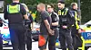 Polizeikräfte stehen neben einem gefesselten Mann vor Einsatzfahrzeugen.