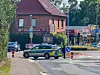 Blau-gelbes Polizeiauto sperrt eine Kreuzung vor einem roten Backsteingebäude.
