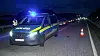 Polizeistreifenwagen mit Blaulicht steht nachts auf einer Fahrbahn neben einer Warnbake.