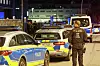 Polizeibeamter steht nachts neben mehreren blau-silbernen Polizeifahrzeugen an einer belebten Straße.