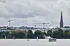 Segelboote und ein Alsterdampfer fahren auf der Außenalster vor Hamburgs Skyline unter dunklen Gewitterwolken.