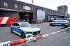 Zwei Polizeiautos sichern eine mit Flatterband abgesperrte Straße vor einem Industriegebäude.