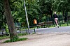 Joggerin läuft im Park an Bäumen, Parkbänken und einem Zaun vorbei.