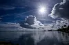 Sonne über dem ruhigen Südpazifik vor Tongas Küste, mit Wolken und Ufervegetation im Gegenlicht.