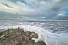 Schaumende Wellen treffen auf einen sandigen Strand unter einem bewölkten Himmel.