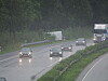 Autos und Lastwagen fahren bei Regen über eine nasse Straße durch einen Wald.