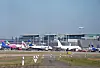 Flugzeuge stehen vor dem Terminal des Hamburg Airport, ein weiteres fliegt über dem Flughafengelände.