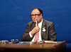 Heinz Erhardt sitzt im Anzug mit Brille und Auszeichnung an einem Schreibtisch vor blauem Hintergrund.