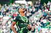Robert Glatzel im grünen Wolfsburg-Trikot blickt im Stadion nach oben, im Hintergrund jubeln Zuschauer.
